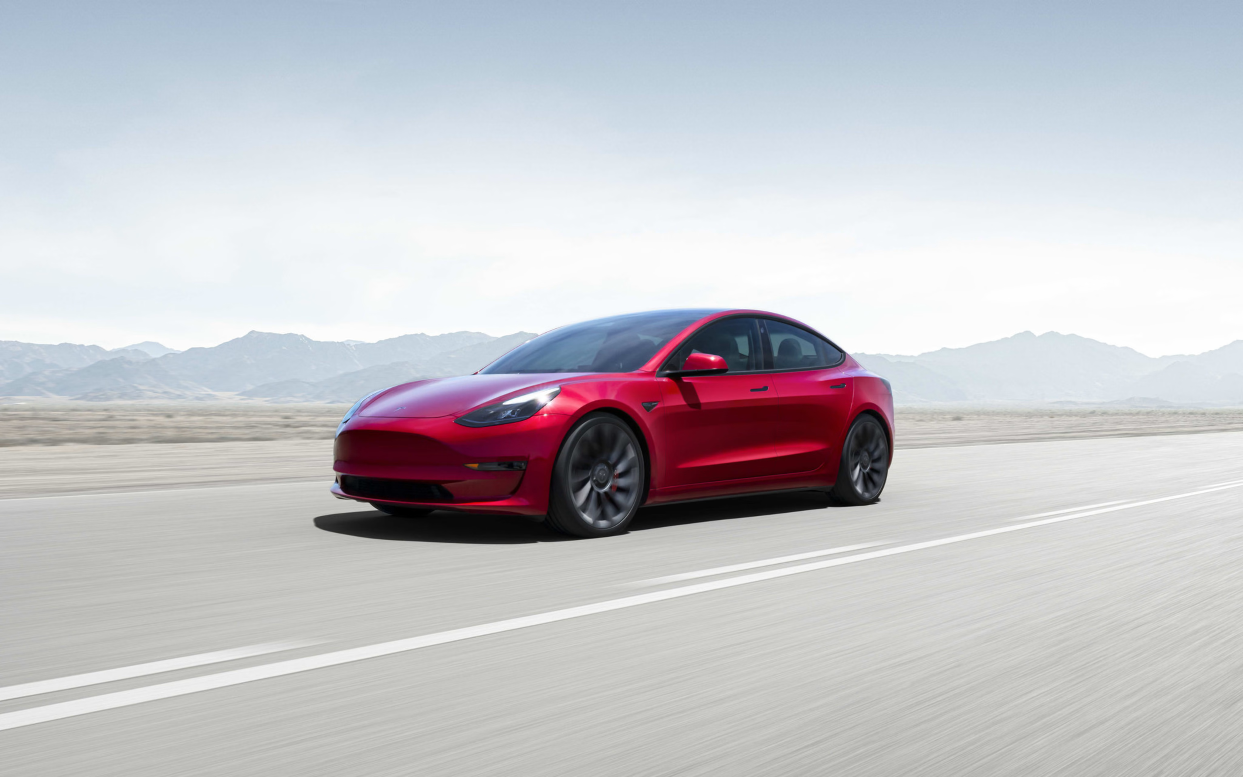 Red Model 3 parked on weathered concrete in front of a cityscape