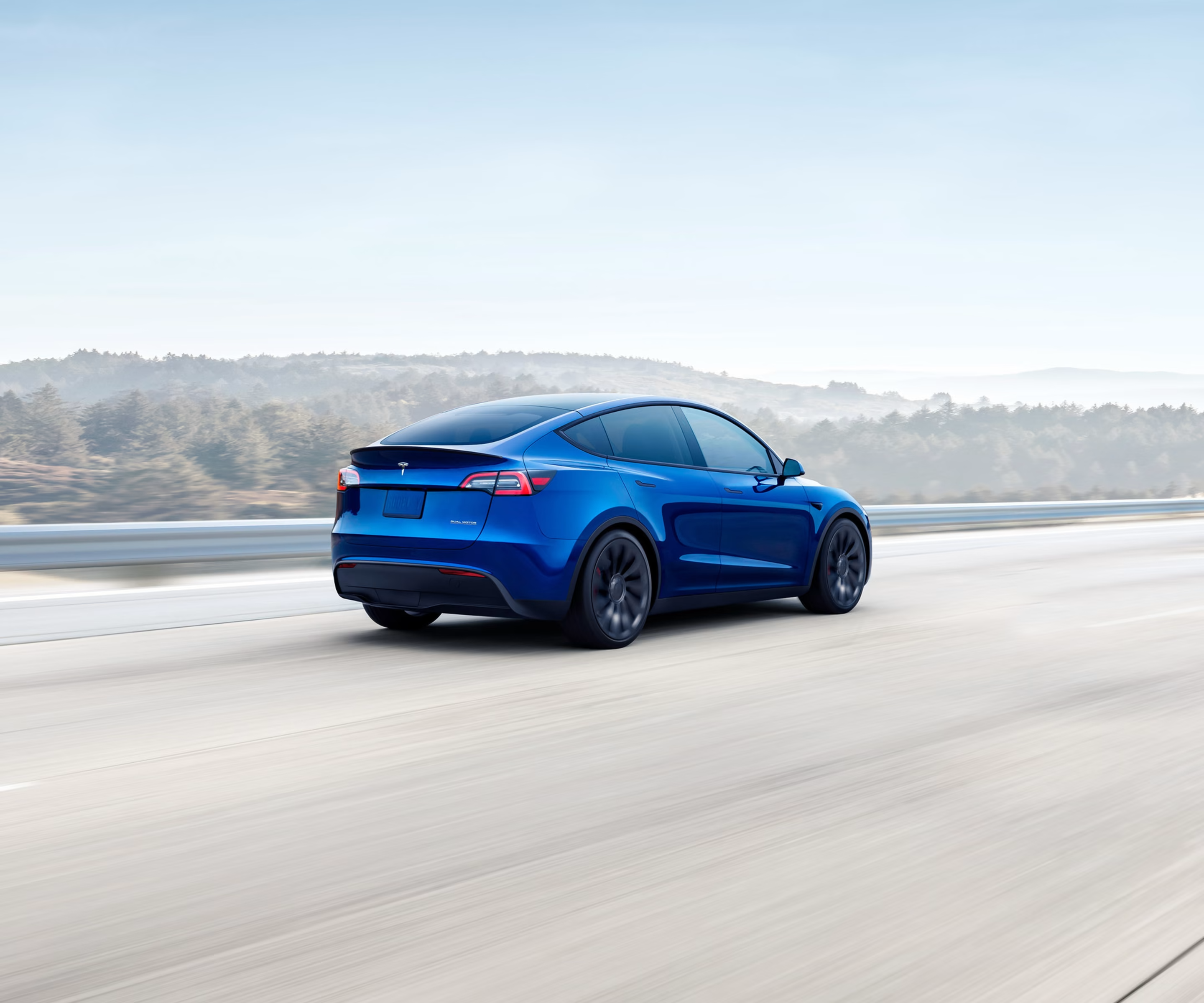 Metallic blue Model Y driving down a hillside highway